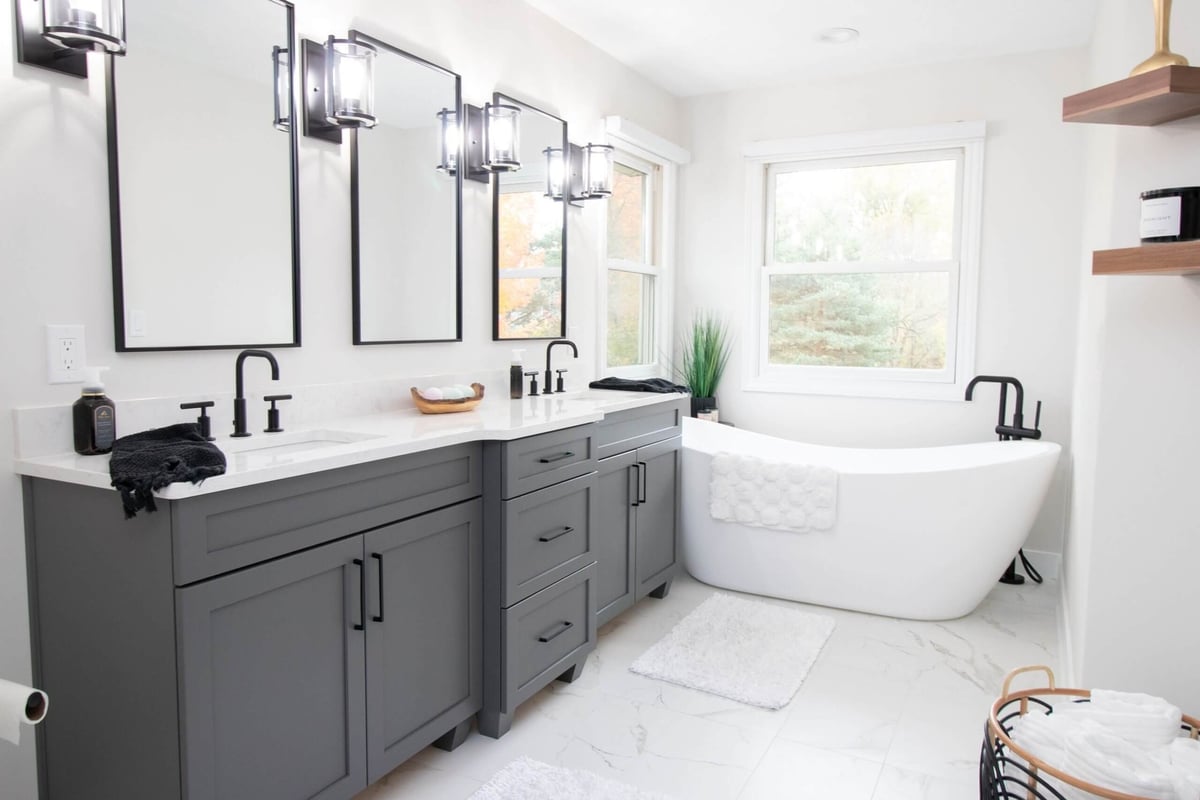 Modern bathroom renovation featuring gray cabinets, dual sinks, and freestanding bathtub by Odd Fellows Contracting in DeWitt, MI.