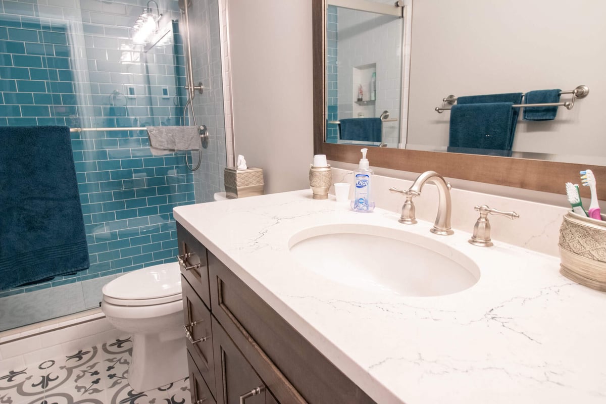 close view of quartz vanity and blue tile shower in a bathroom remodel by Odd Fellows Contracting in Williamston, MI