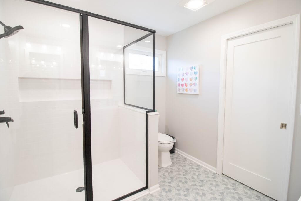walk-in shower with black framed glass and hex tile flooring from bathroom remodel by Odd Fellows Contracting in Okemos, MI