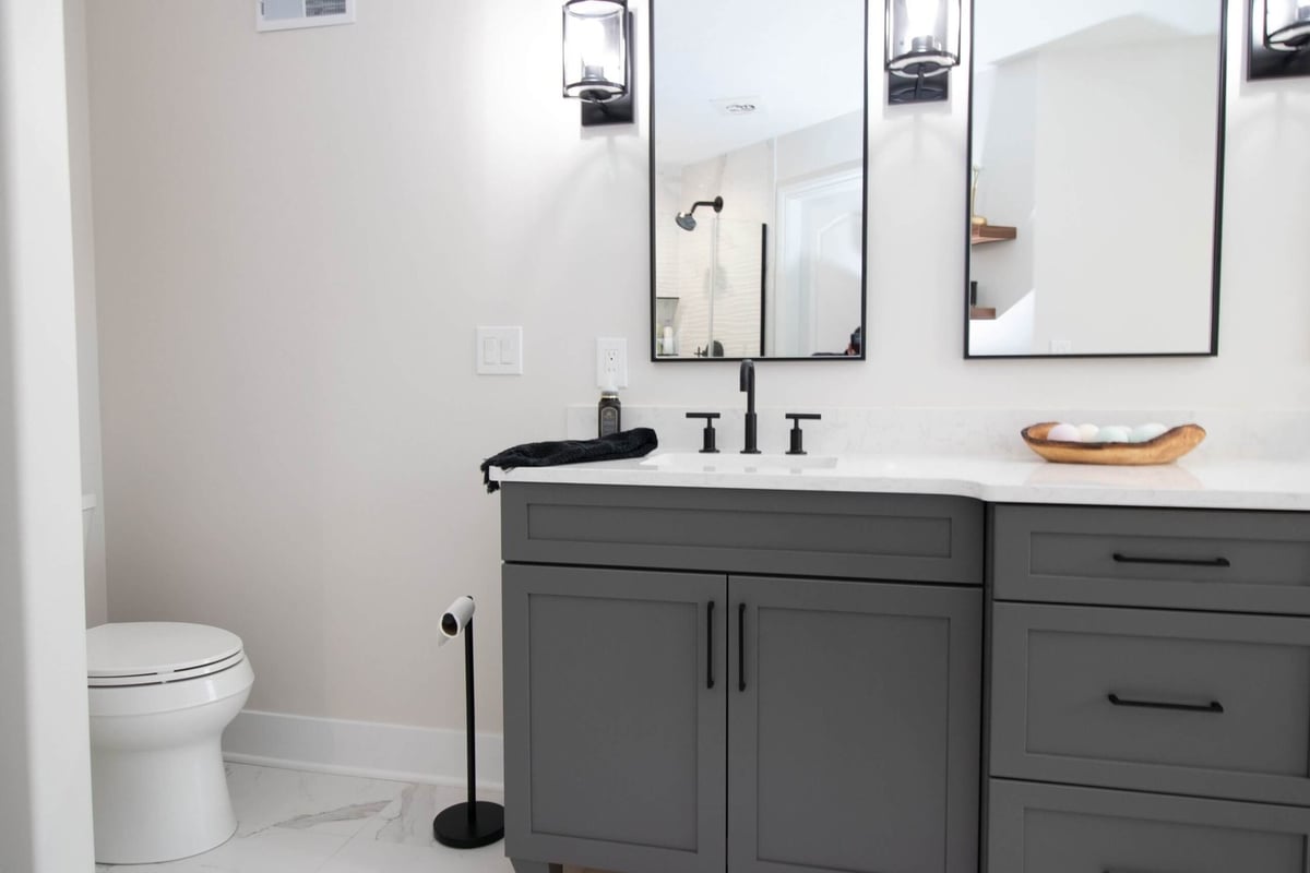Bathroom remodel vanity with gray cabinets, dual sinks, and modern black fixtures by Odd Fellows Contracting in DeWitt, MI.