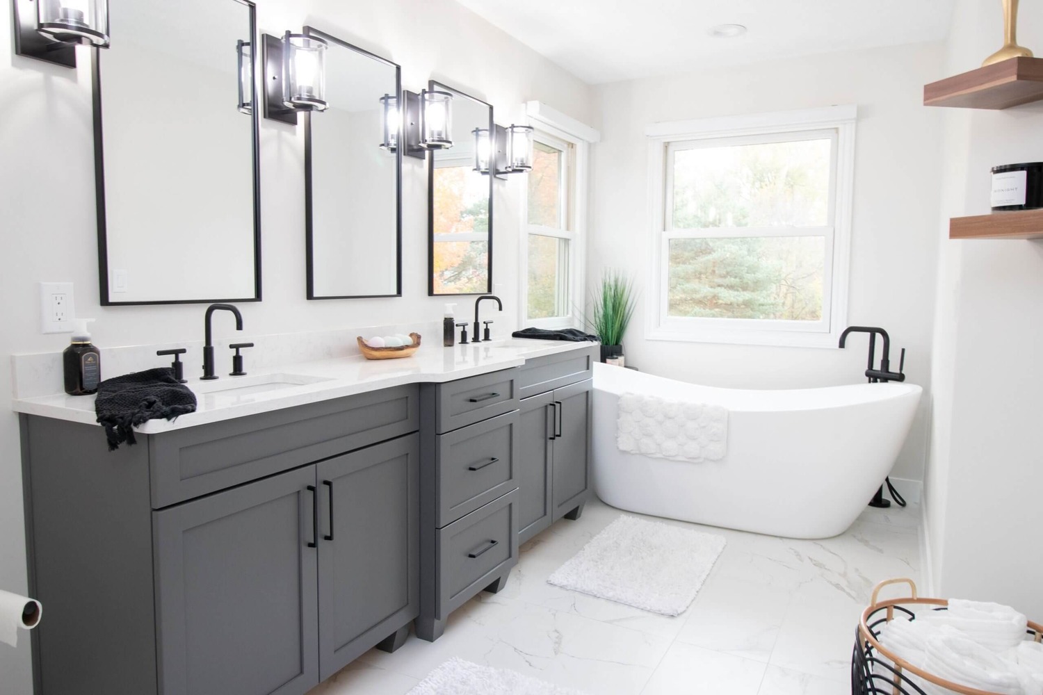 Modern bathroom renovation featuring gray cabinets, dual sinks, and freestanding bathtub by Odd Fellows Contracting in DeWitt, MI.