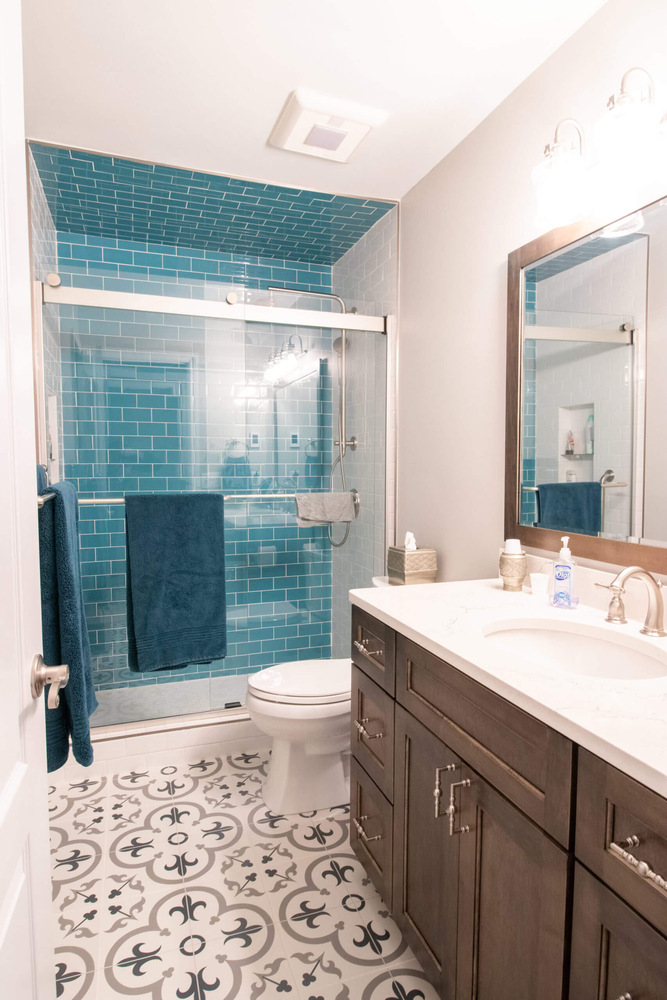 bright bathroom remodel with glass shower enclosure, blue subway tile walls, and patterned floor tile by Odd Fellows Contracting in Williamston, MI