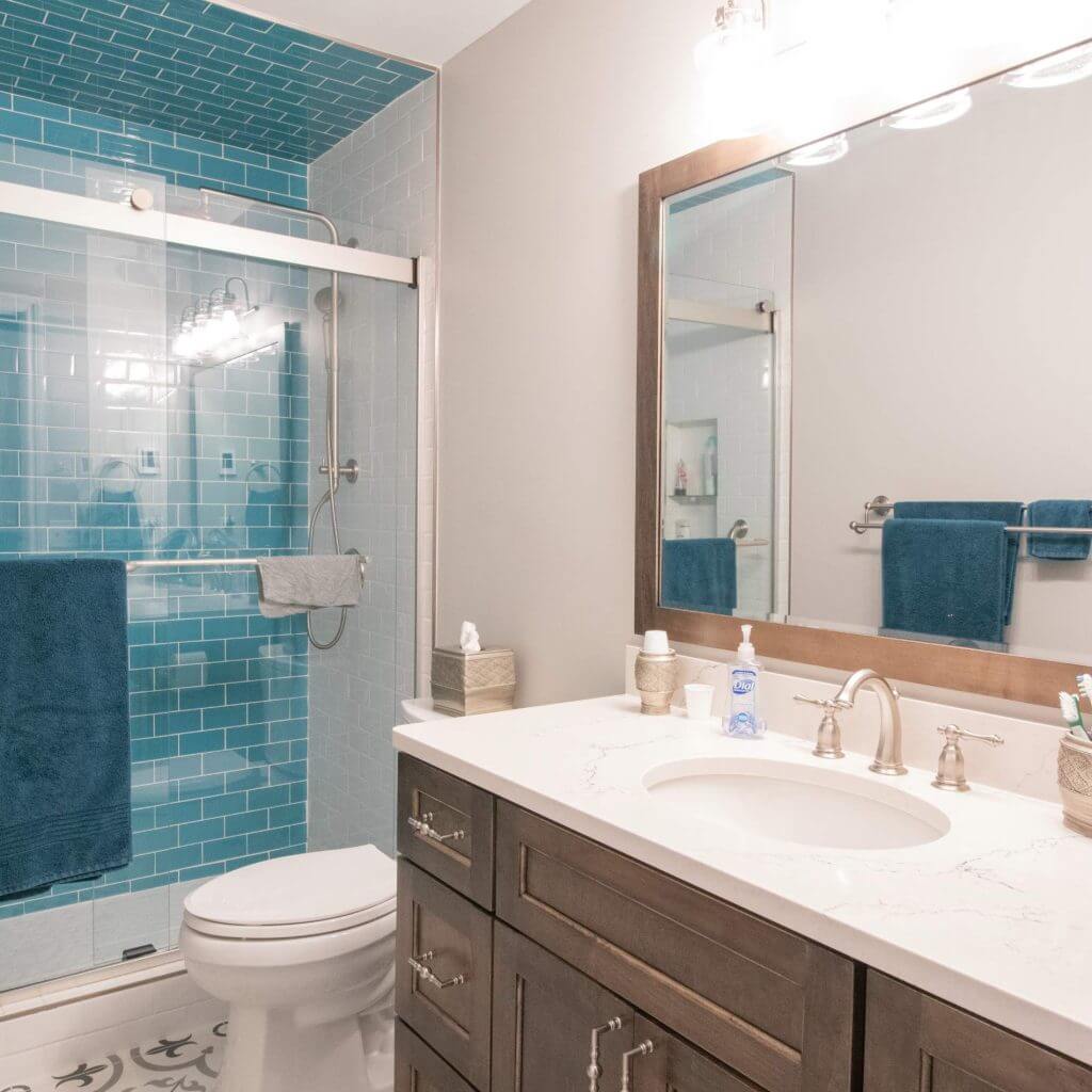 modern bathroom remodel with blue subway tile shower, quartz vanity, and patterned tile floor by Odd Fellows Contracting in Williamston, MI