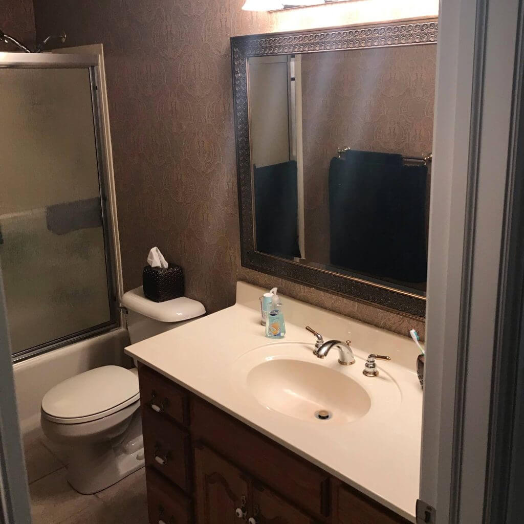 original bathroom before remodel with outdated vanity, mirror, and tub shower combo in Williamston, MI by Odd Fellows Contracting