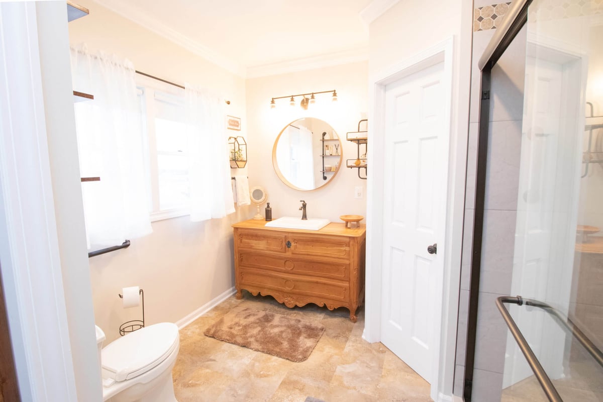 bright remodeled bathroom with vanity cabinet, round mirror, and glass walk in shower by Odd Fellows Contracting in Webberville, MI
