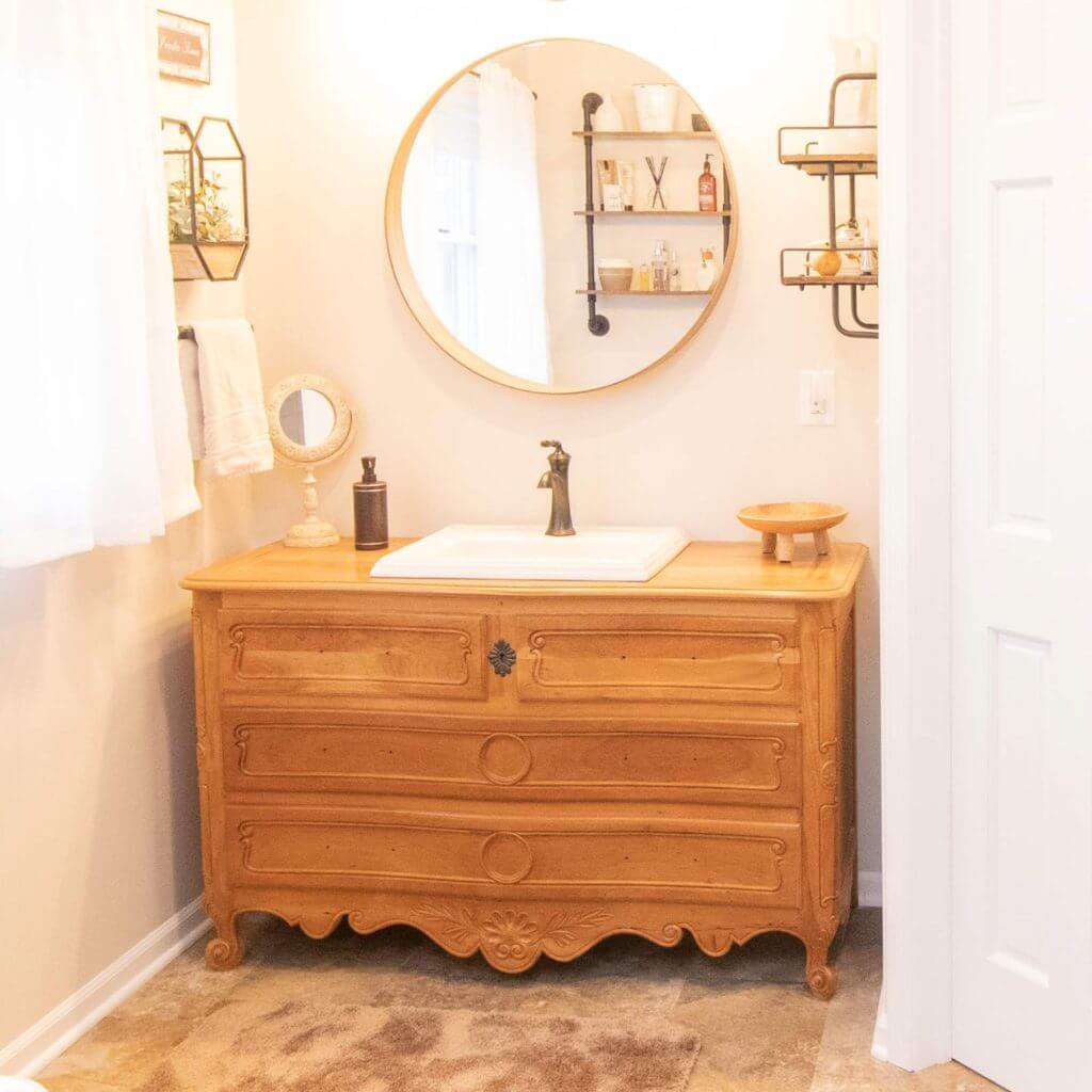 remodeled bathroom vanity with wood dresser style cabinet and round mirror by Odd Fellows Contracting in Webberville, MI