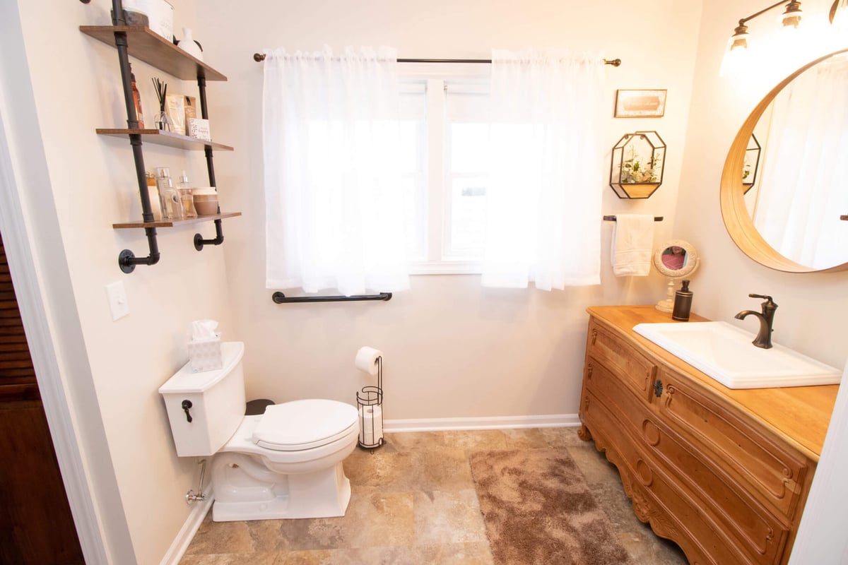 remodeled bathroom with dresser style vanity, round mirror, and decorative shelving by Odd Fellows Contracting in Webberville, MI