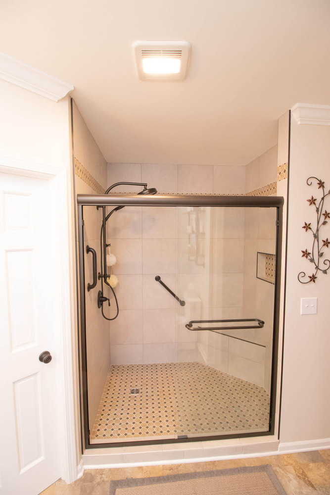 spacious walk in shower with tile walls, mosaic floor, and grab bars in bathroom remodel by Odd Fellows Contracting in Webberville, MI