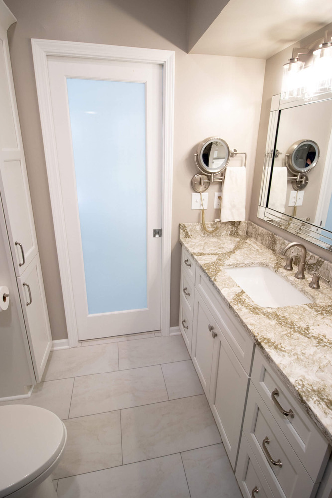 bathroom remodel vanity with granite countertop, framed mirror, and frosted glass door by Odd Fellows Contracting in Williamston, MI