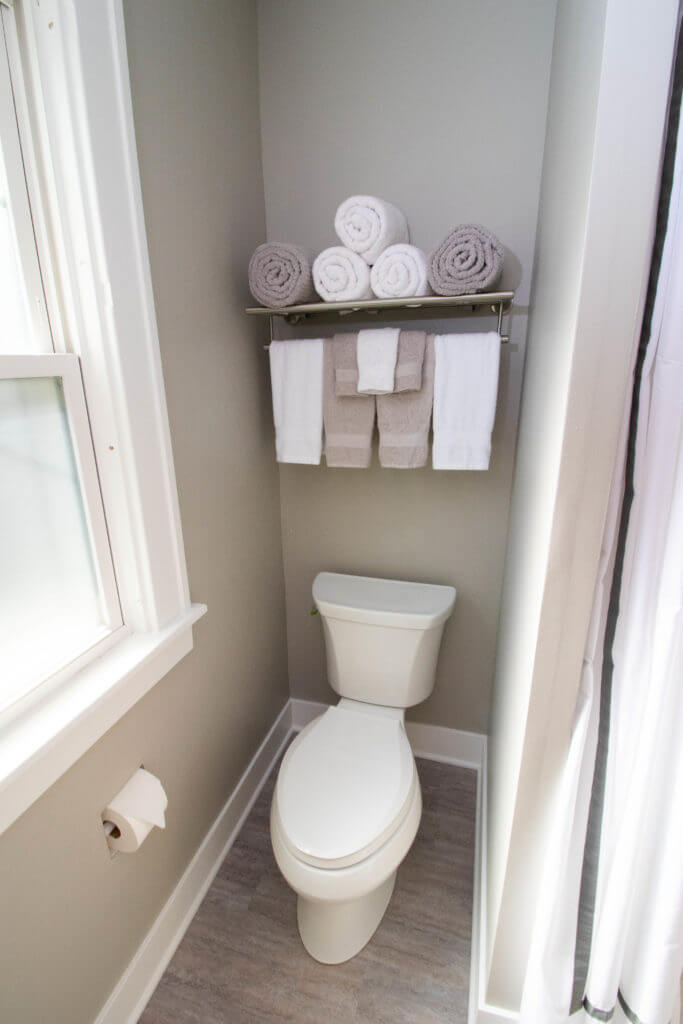compact bathroom toilet area by Odd Fellows Contracting in East Lansing MI with shelving and towel storage