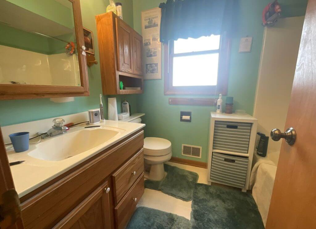 before bathroom remodel by Odd Fellows Contracting in Williamston, MI featuring dated wood vanity and green walls