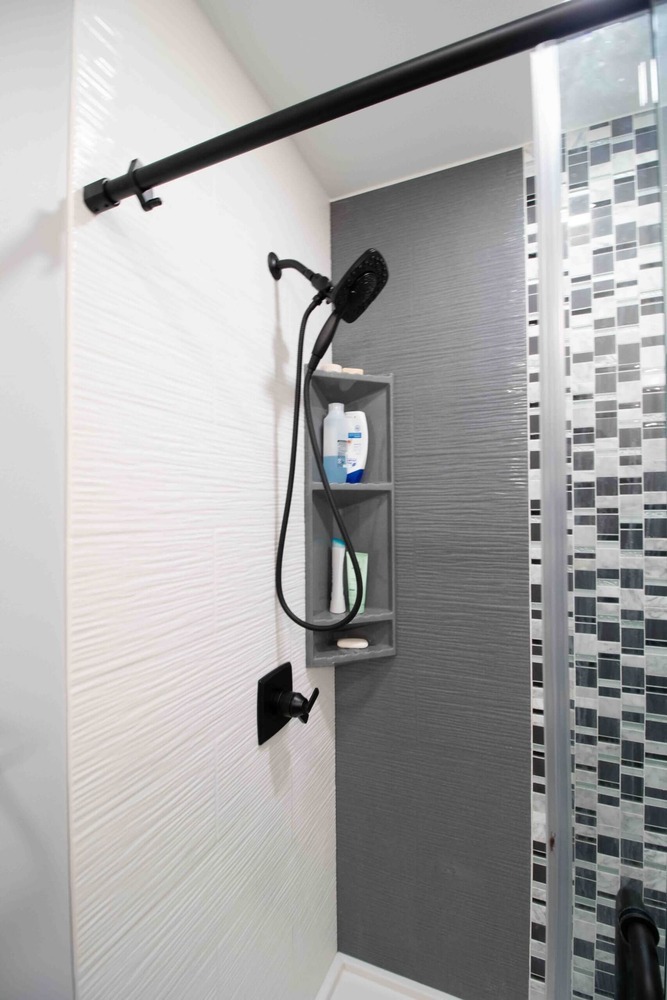 remodeled shower with glass enclosure black fixtures and tile accent wall by Odd Fellows Contracting in Okemos MI
