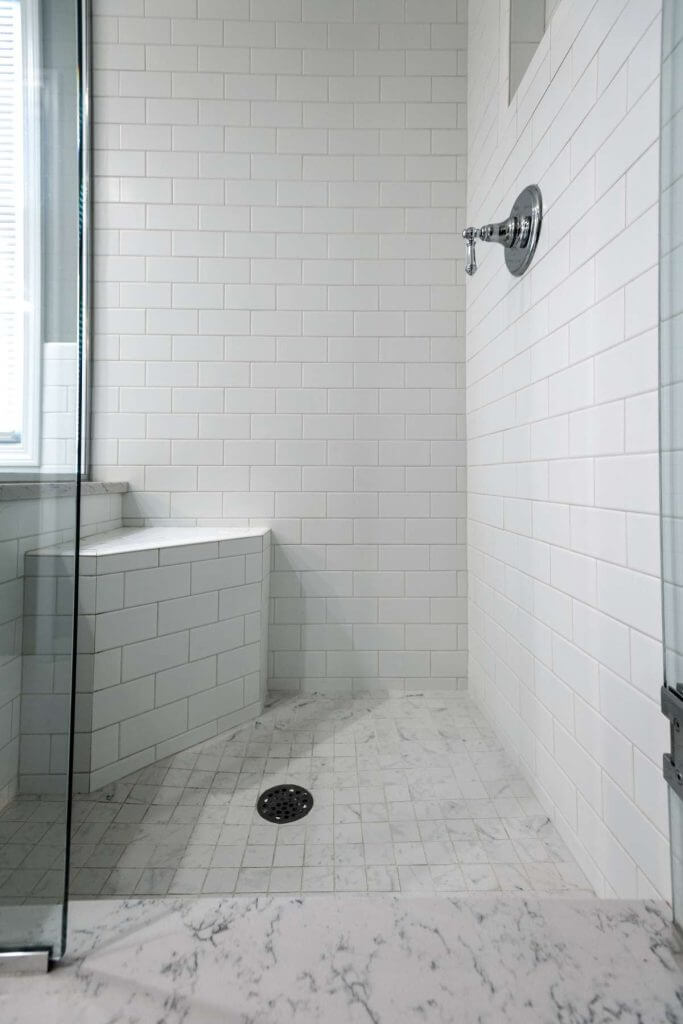 Walk-in shower with white subway tile and marble floor in master bathroom remodel by Odd Fellows Contracting in Williamston, MI
