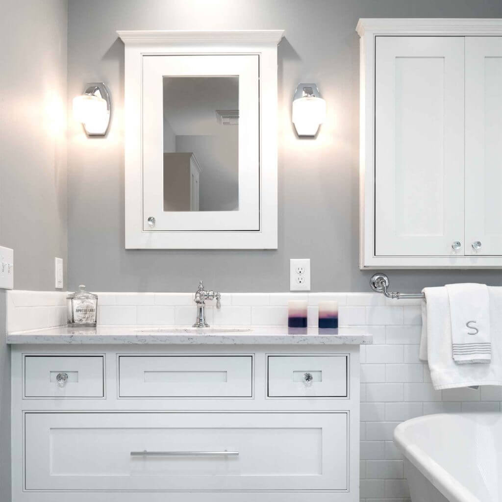White vanity with quartz countertop and wall sconces in a master bathroom remodel by Odd Fellows Contracting in Williamston, MI