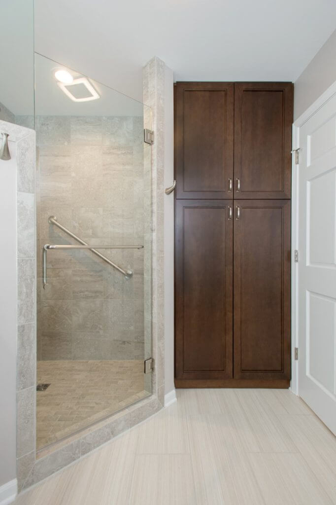 Glass walk-in shower and custom storage cabinets in Holt MI bathroom remodel by Odd Fellows Contracting