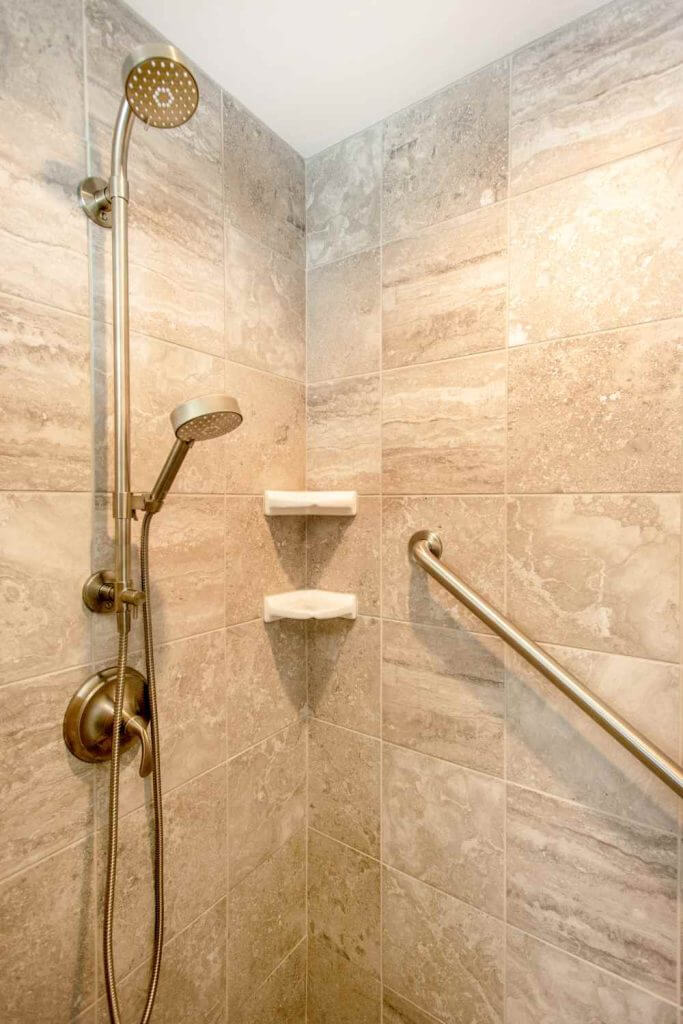 Tile shower with dual shower heads and corner shelves in Holt MI bathroom remodel by Odd Fellows Contracting