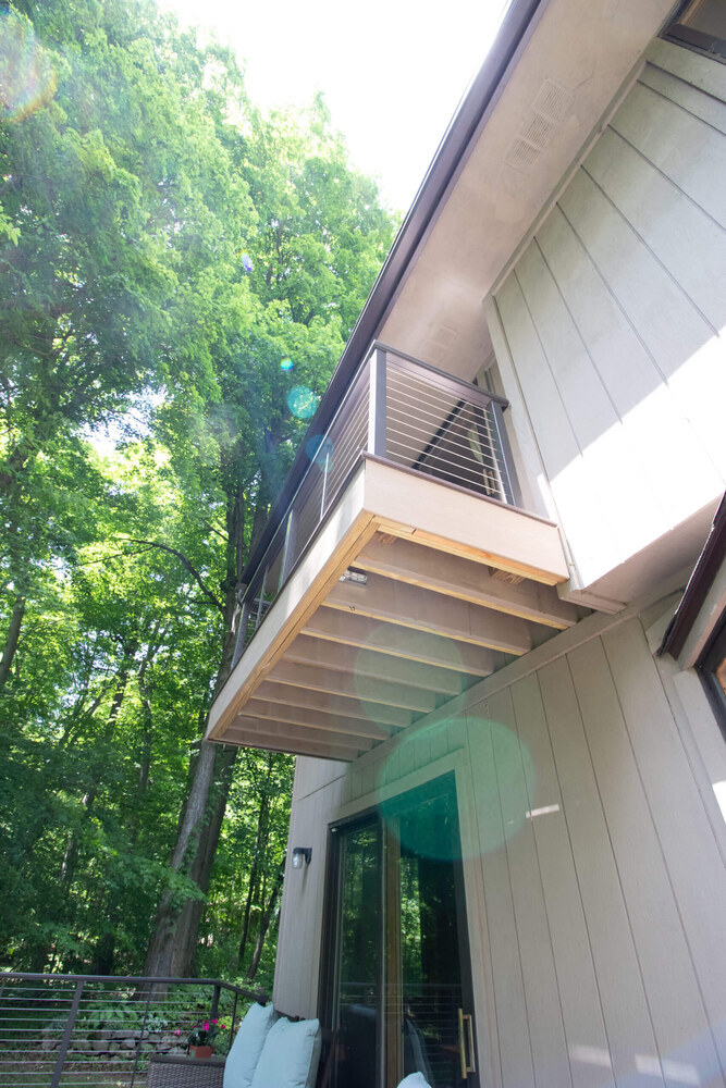 Composite deck seating area overlooking wooded backyard by Odd Fellows Contracting in Mason, MI