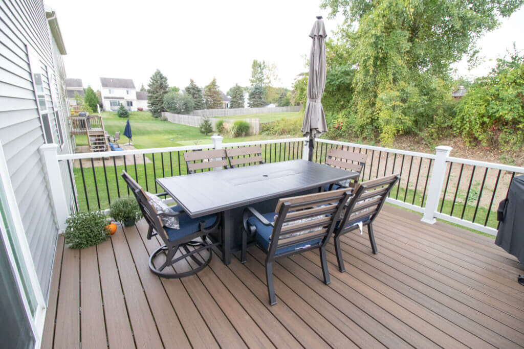 composite deck with outdoor dining set and railing overlooking backyard by Odd Fellows Contracting in Williamston, MI