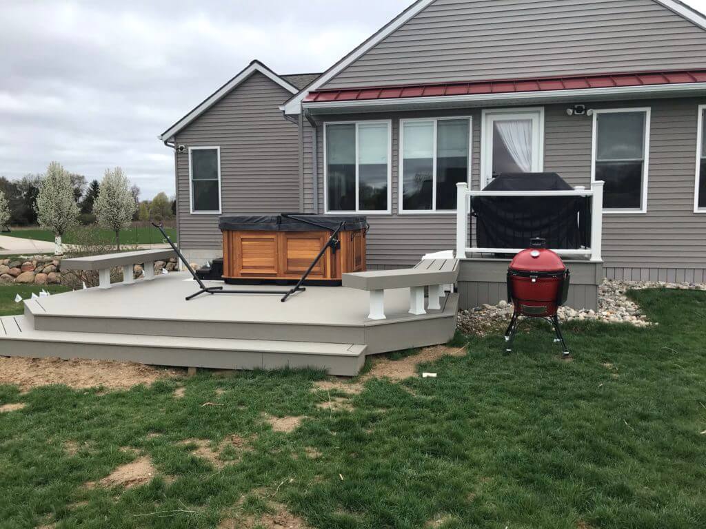 Composite deck extension with hot tub and built-in seating by Odd Fellows Contracting in Haslett MI