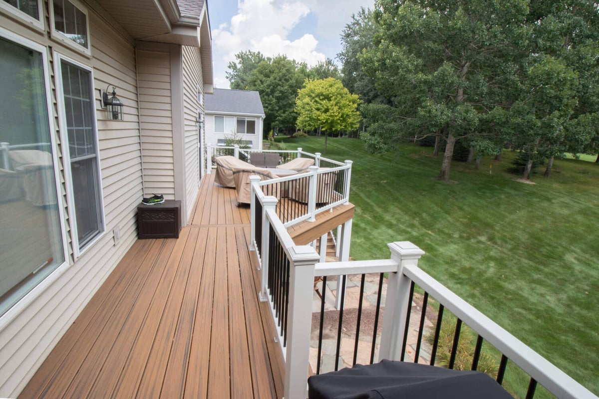 backyard deck renovation featuring composite decking, white posts, and black baluster railings by Odd Fellows Contracting in Williamston, MI