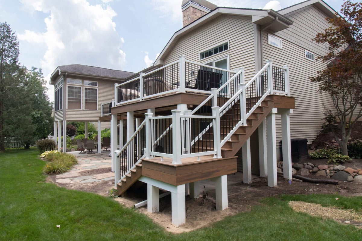 composite deck remodel with wide staircase and modern white railing system by Odd Fellows Contracting in Williamston, MI