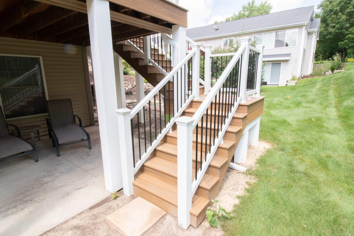 composite deck staircase remodel with white railing posts and black balusters by Odd Fellows Contracting in Williamston, MI
