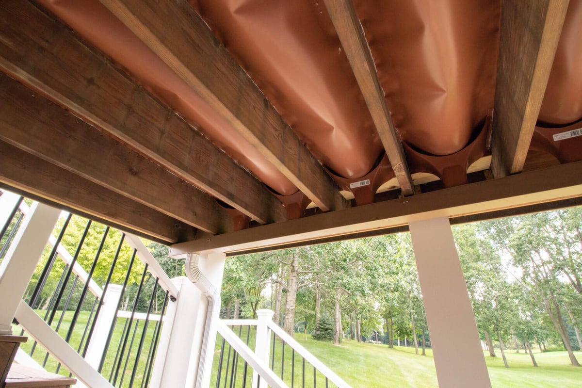 underside view of composite deck framing and drainage system during deck remodel by Odd Fellows Contracting in Williamston, MI