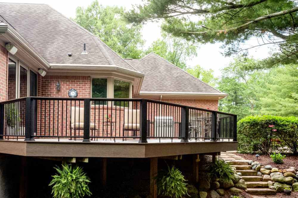 Elevated composite deck with black railing attached to brick home in Williamston MI by Odd Fellows Contracting