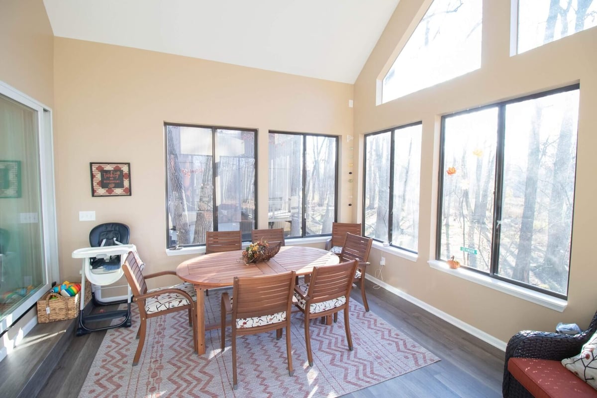 sunroom interior with dining table and panoramic forest views by Odd Fellows Contracting in Haslett MI