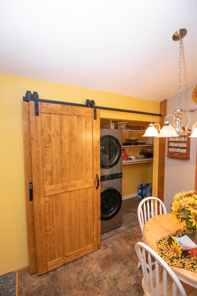 Sliding barn door opening to reveal stacked washer and dryer in garage laundry addition by Odd Fellows Contracting in Williamston, MI