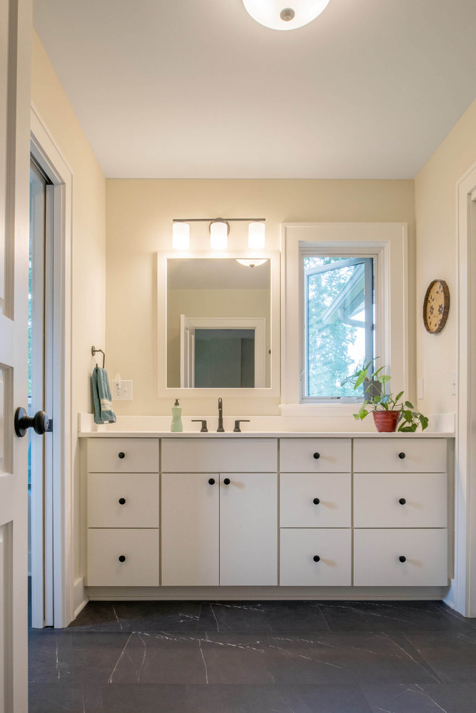 Double vanity bathroom addition with white cabinets and black tile flooring by Odd Fellows Contracting in Mason, MI