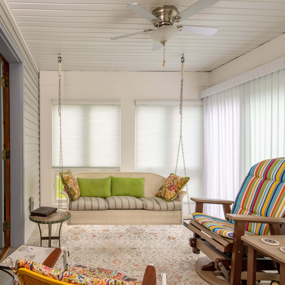 Three seasons room seating area with swing sofa and large windows by Odd Fellows Contracting in Holt, MI