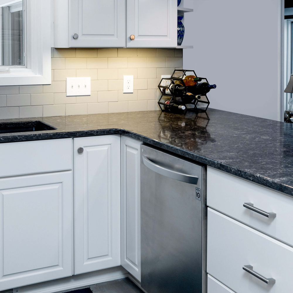 Corner kitchen remodel detail with white cabinets, dark countertops, and stainless dishwasher by Odd Fellows Contracting in Haslett, MI