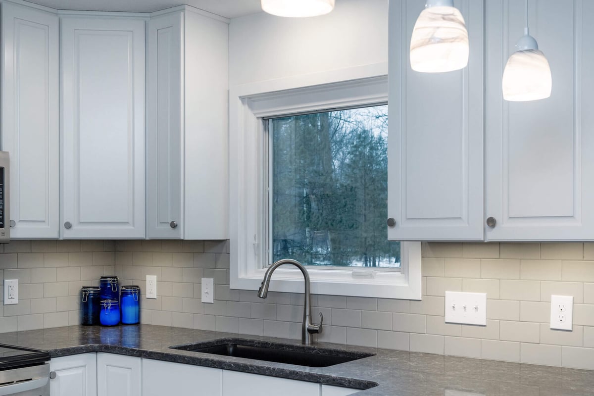 Kitchen remodel detail with window sink, tile backsplash, and modern faucet by Odd Fellows Contracting in Haslett, MI