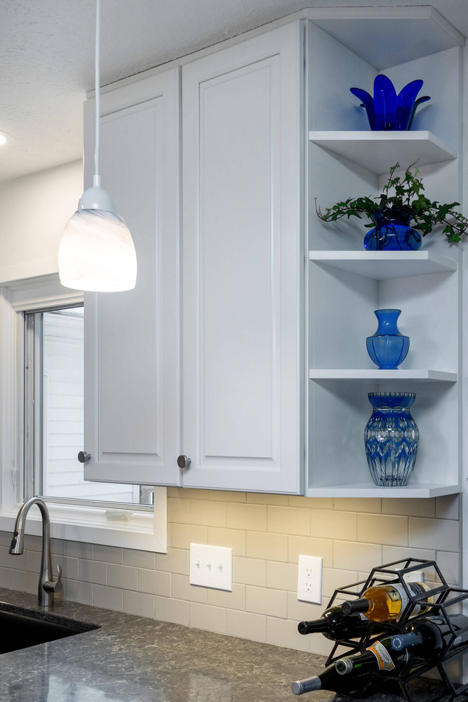 Remodeled kitchen cabinet wall with open shelving and decorative blue glass accents by Odd Fellows Contracting in Haslett, MI
