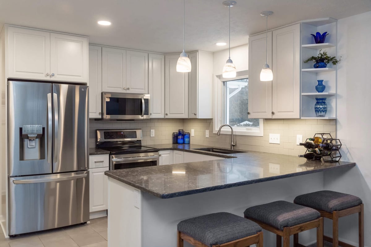 Remodeled kitchen with white cabinetry, pendant lights, and island by Odd Fellows Contracting in Haslett, MI