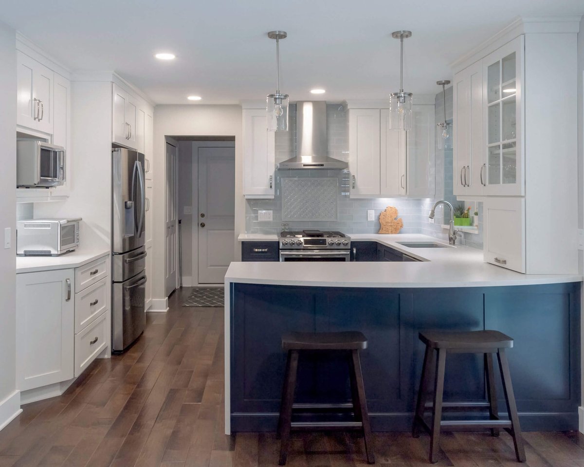 Bright remodeled kitchen with white cabinets, blue island base, and stainless appliances by Odd Fellows Contracting in Okemos, MI