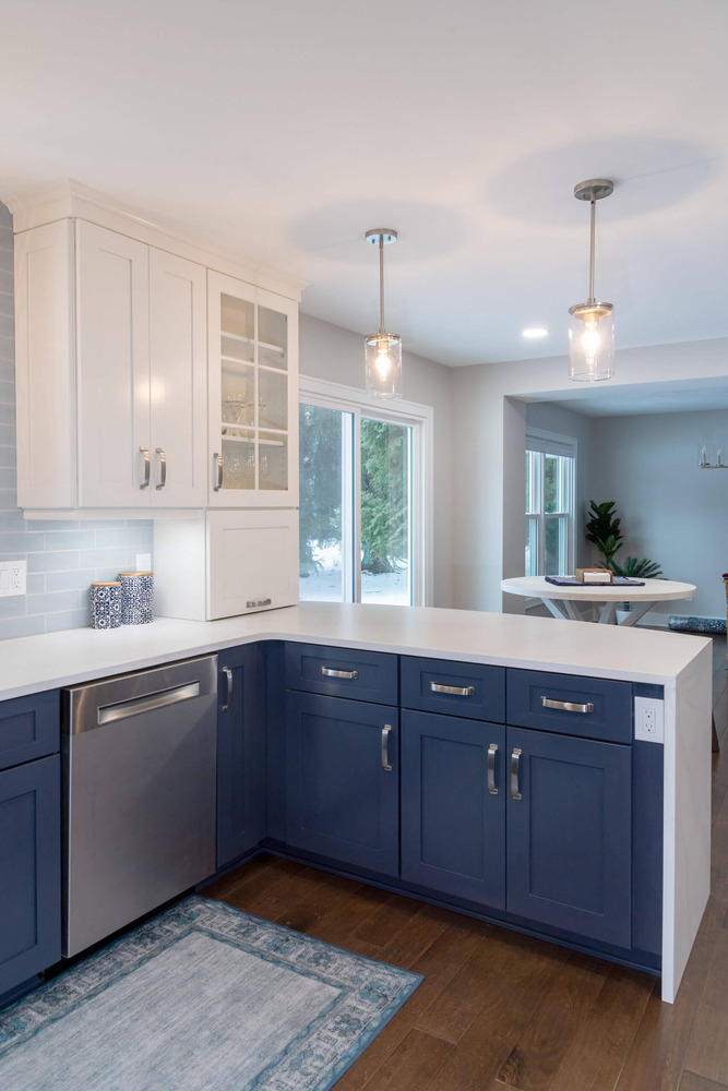 Updated kitchen remodel with white cabinetry, blue lower cabinets, and quartz peninsula by Odd Fellows Contracting in Okemos, MI
