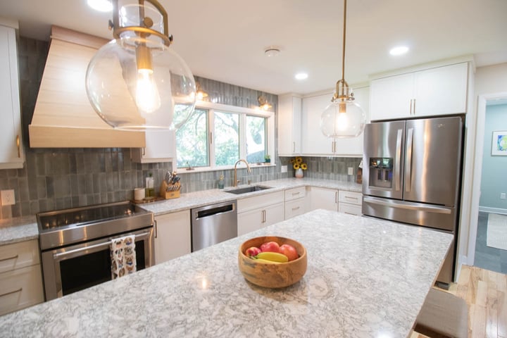 completed kitchen remodel by Odd Fellows Contracting in Hiawatha Lakes, Okemos, MI showcasing large quartz island and custom wood range hood