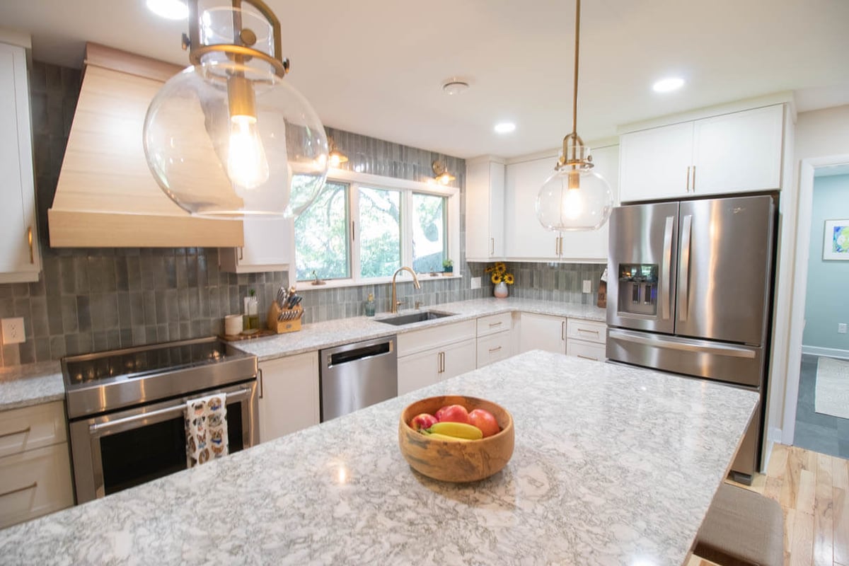 completed kitchen remodel by Odd Fellows Contracting in Hiawatha Lakes, Okemos, MI showcasing large quartz island and custom wood range hood
