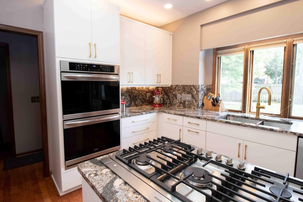 remodeled kitchen with large island cooktop granite countertops and white cabinets by Odd Fellows Contracting in Lansing MI