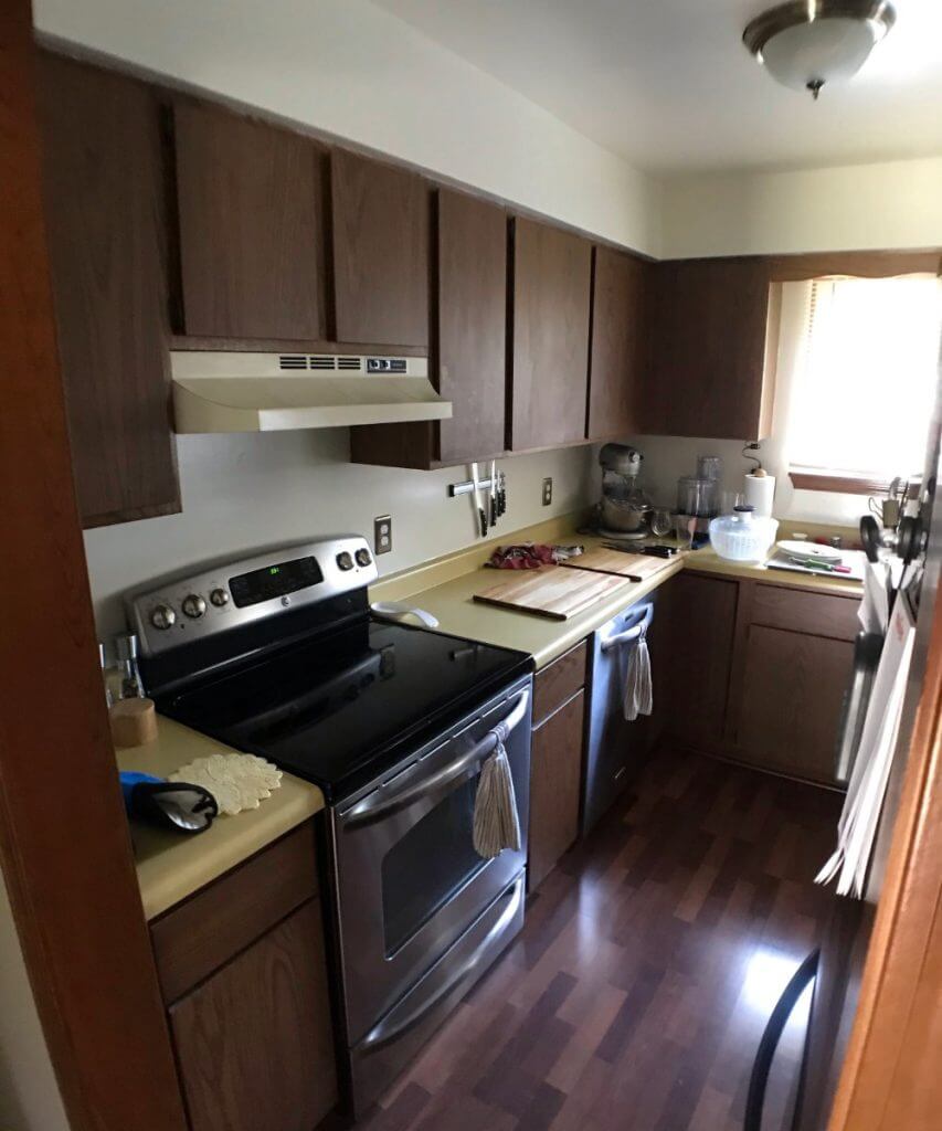 Before photo of outdated kitchen with dark wood cabinets and laminate countertops prior to remodel by Odd Fellows Contracting in Lansing, MI.