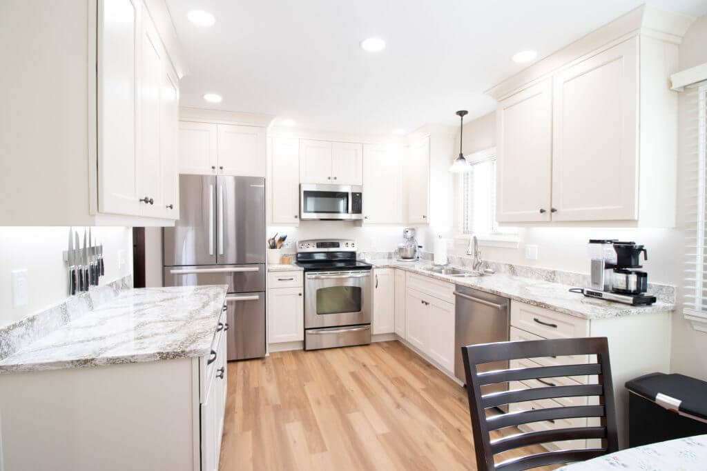 Bright remodeled kitchen with white cabinets, granite countertops, and stainless appliances by Odd Fellows Contracting in Lansing, MI.