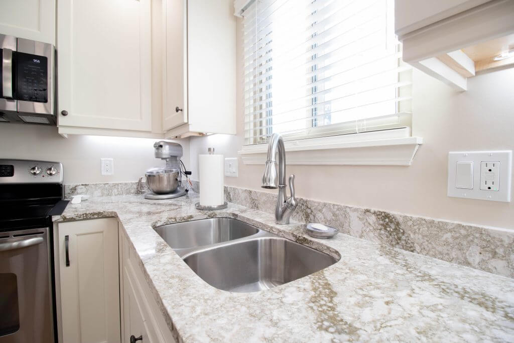 Close-up of remodeled kitchen sink with granite countertop and stainless fixtures by Odd Fellows Contracting in Lansing, MI.