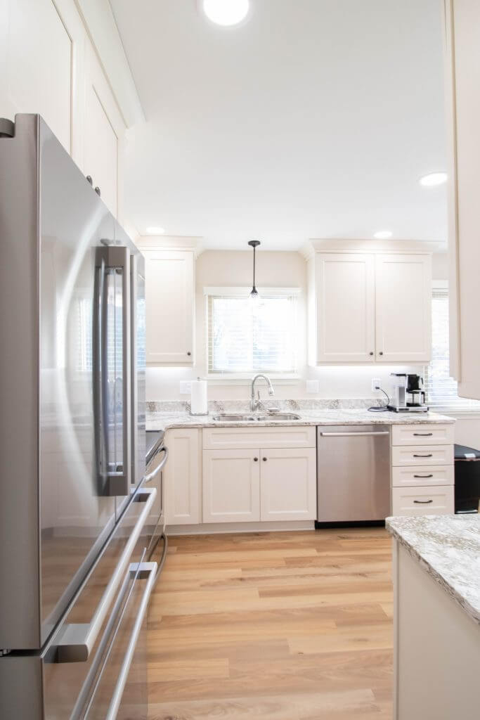Kitchen remodel view with stainless refrigerator, white cabinets, and granite countertops by Odd Fellows Contracting in Lansing, MI.