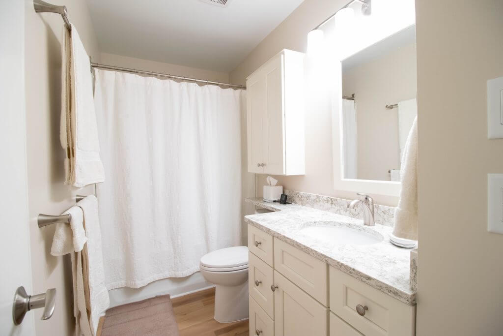 Updated bathroom with granite vanity top, white cabinets, and tub shower by Odd Fellows Contracting in Lansing, MI.