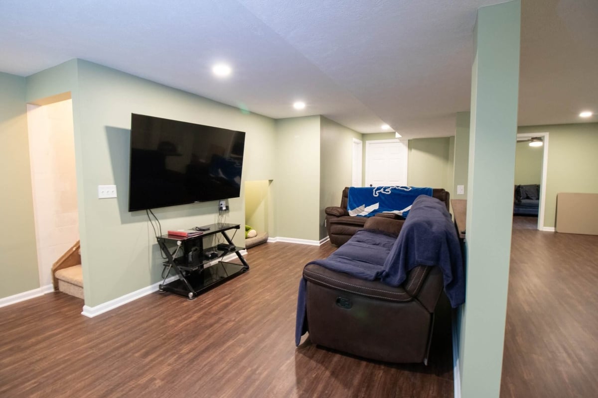 Basement remodel entertainment area with seating and wall-mounted TV by Odd Fellows Contracting in Lansing, MI.