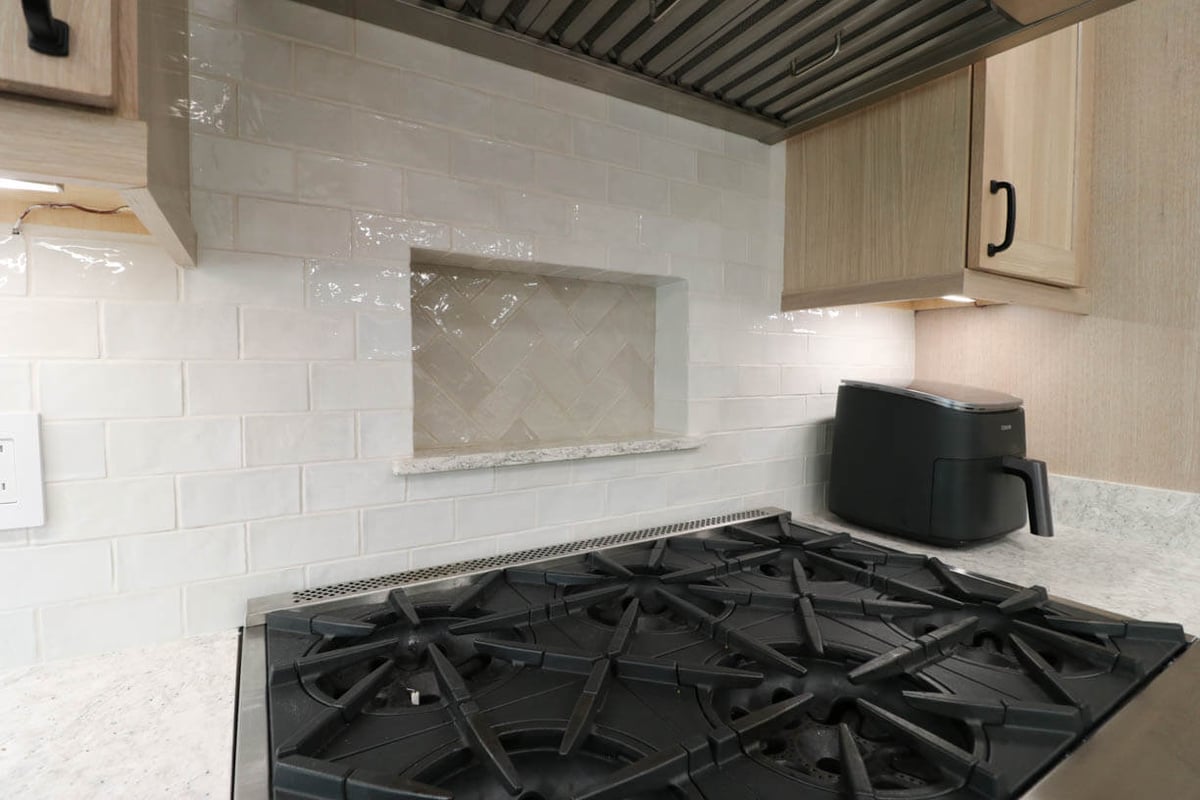 Kitchen design detail in Cornell Woods, MI custom home by Odd Fellows Contracting with herringbone tile accent and gas cooktop.