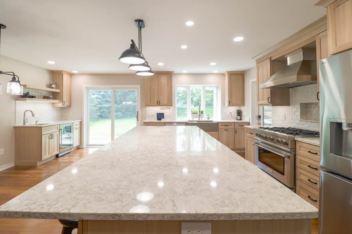Open-concept custom home kitchen by Odd Fellows Contracting in Cornell Woods, MI with quartz countertops and hardwood flooring.