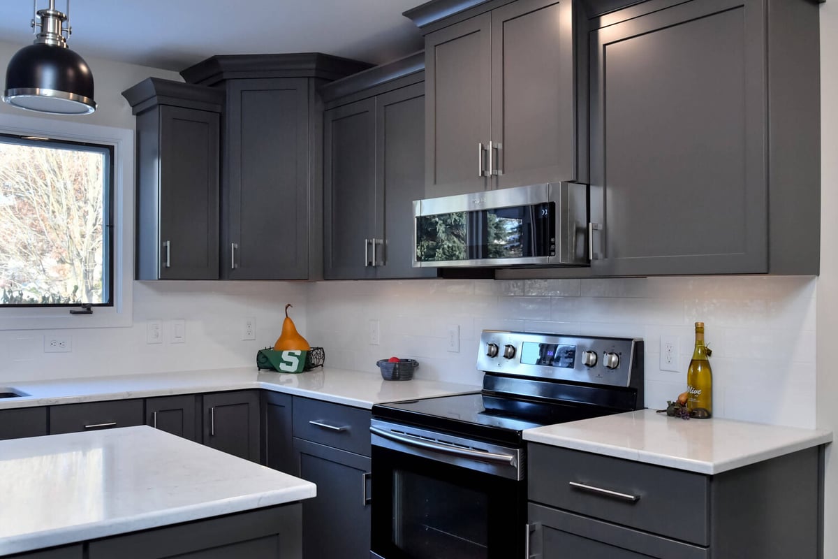 Modern kitchen cooking area with gray cabinets and stainless range by Odd Fellows Contracting in Okemos, MI
